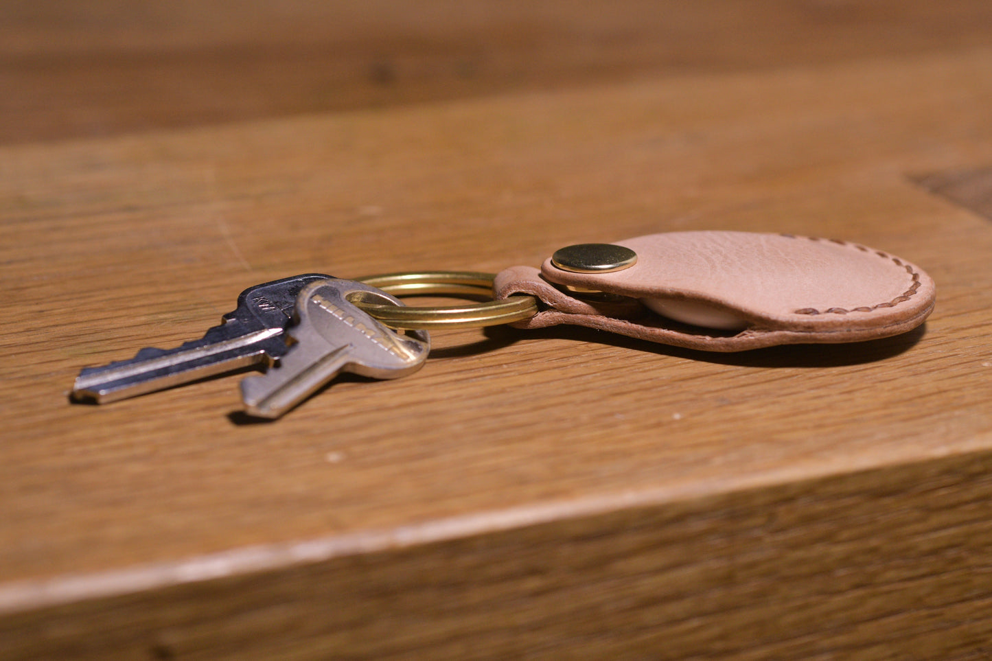 AirTag holder with brass keychain ring, natural veg tan leather, hand made (side profile with keys attached)