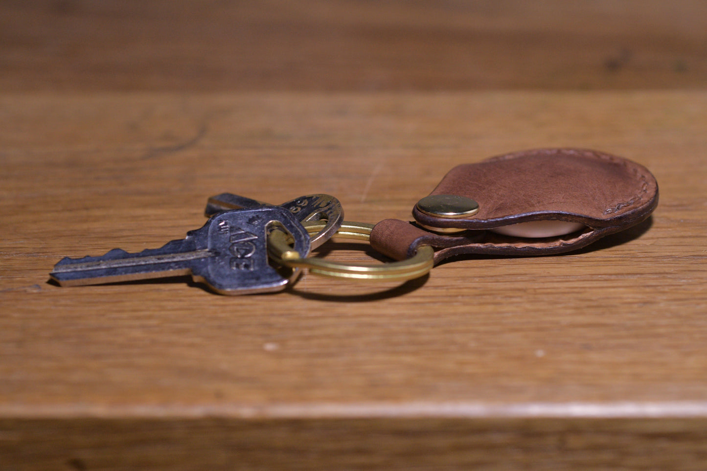AirTag holder with brass keychain ring, brown veg tan leather, hand made (side profile with keys attached)